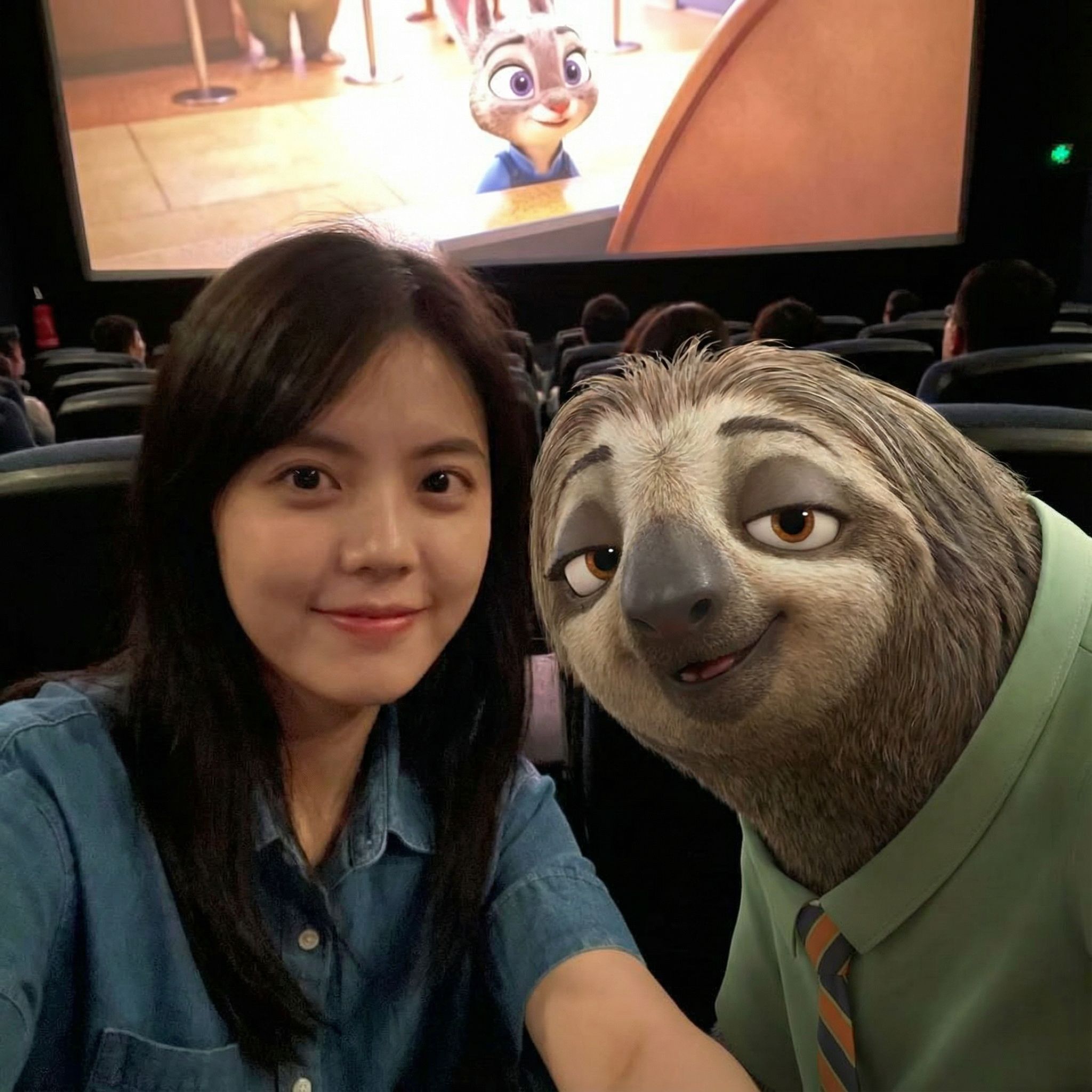 Create an ultra-realistic selfie photo. Use my uploaded image as the exact reference for the real person — do not modify, change, or adjust any features of the person from the uploaded image.

Add Flash the sloth from Zootopia (Disney character) standing next to this real person.

Scene: A dark, crowded movie theater. In the background, a large screen is playing a scene from Zootopia. Cinematic lighting with warm ambient tones.

Composition: Selfie angle. The real person from Image 1 (keep all original features exactly the same) and Flash taking a selfie together, both smiling and looking at the camera. Both subjects are in sharp focus. Ultra-high definition, 8K quality, hyper-realistic photography style, natural lighting mixed with screen glow, shallow depth of field.

Key requirement: The real person must look exactly the same as in my uploaded image — do not change her hairstyle, clothing, accessories, or any facial features. Only add the Zootopia character into the scene.